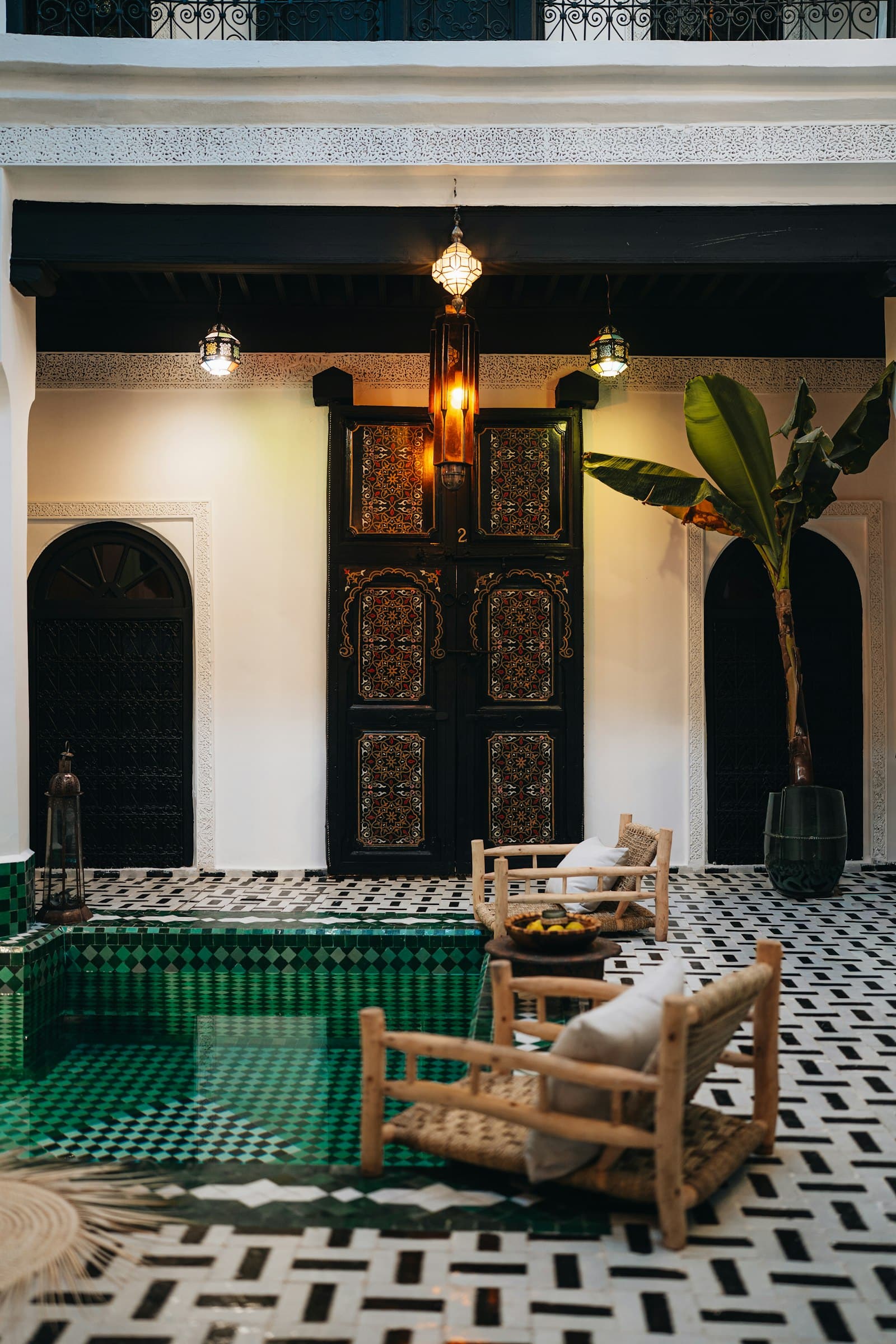 Small tiled pool in a white courtyard with wooden chairs and a carved door (placeholder photo)